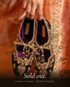 Hand holding a pair of Amanat velvet embroidered ballet juttis with beaded tassels, Sold out banner, Coral Haze