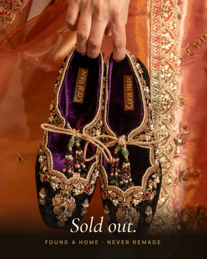 Hand holding a pair of Amanat velvet embroidered ballet juttis with beaded tassels, Sold out banner, Coral Haze