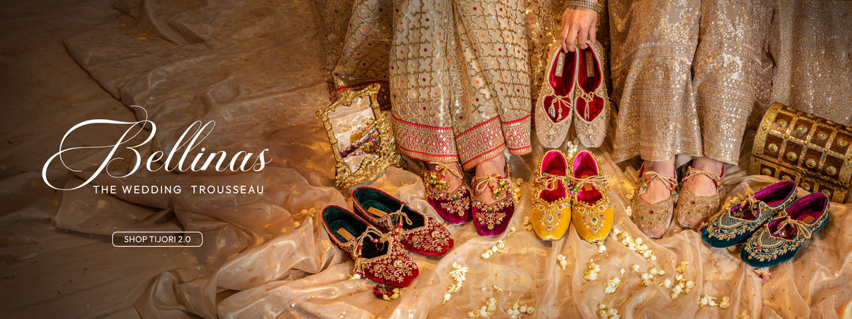 Wide banner of colorful embellished bridal juttis arranged on gold cream fabric with wedding jewelry boxes, text: Bellinas The Wedding Trousseau, Shop Now, Coral Haze